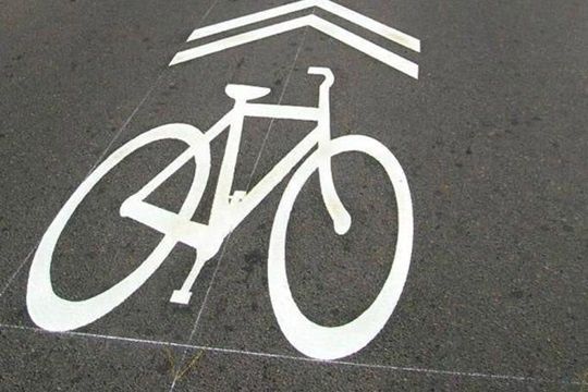 Vit cykelsymbol och väjningsmarkering målad på mörk asfalt