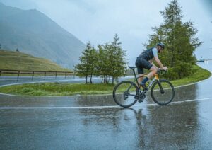 Cyklist trampar på en våt väg i kraftigt regn bland berg och träd