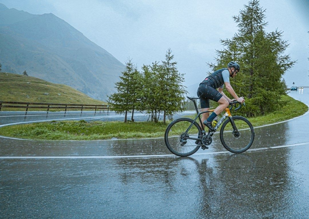 Cyklist trampar på en våt väg i kraftigt regn bland berg och träd