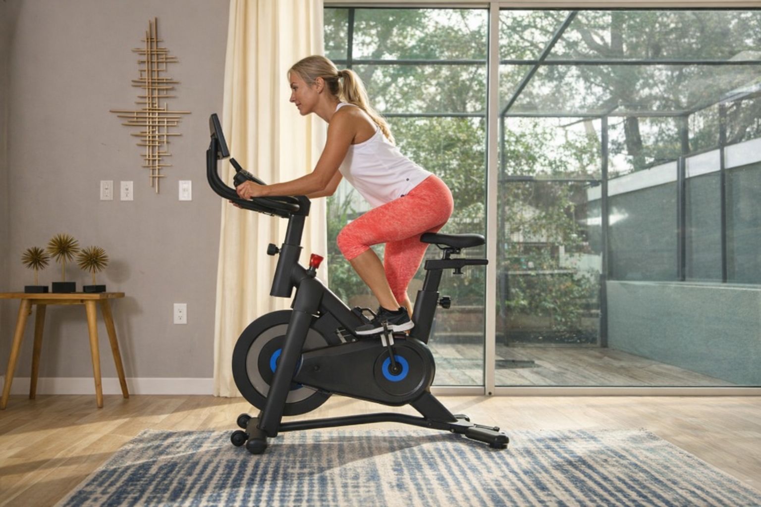 Kvinna som tränar på en modern svart motionscykel i ett ljust vardagsrum.